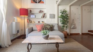 A living room with a sofa, a coffee table with a plant, a red lamp, a bookshelf, and a potted plant. - Cozy and modern studio apartment by Mmega (Florence)