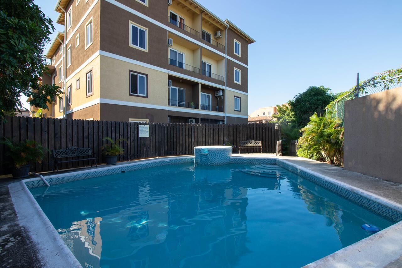 A rectangular swimming pool with a wooden deck and a hot tub, surrounded by a wooden fence.