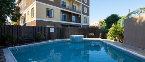 A rectangular swimming pool with a wooden deck and a hot tub, surrounded by a wooden fence.