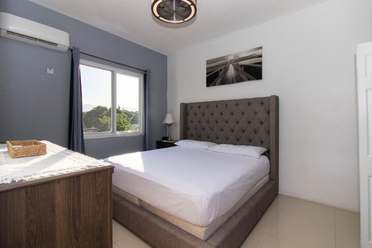A bedroom with a large bed, a bedside table, a lamp, and a window with curtains.