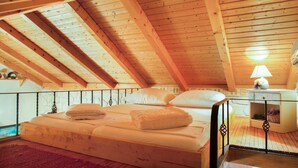 A bedroom with a wooden ceiling, a bed with pillows and a blanket, a nightstand with a lamp, and a stone wall. - Holiday house Jano in Makarska, jacuzzi (Makarska)