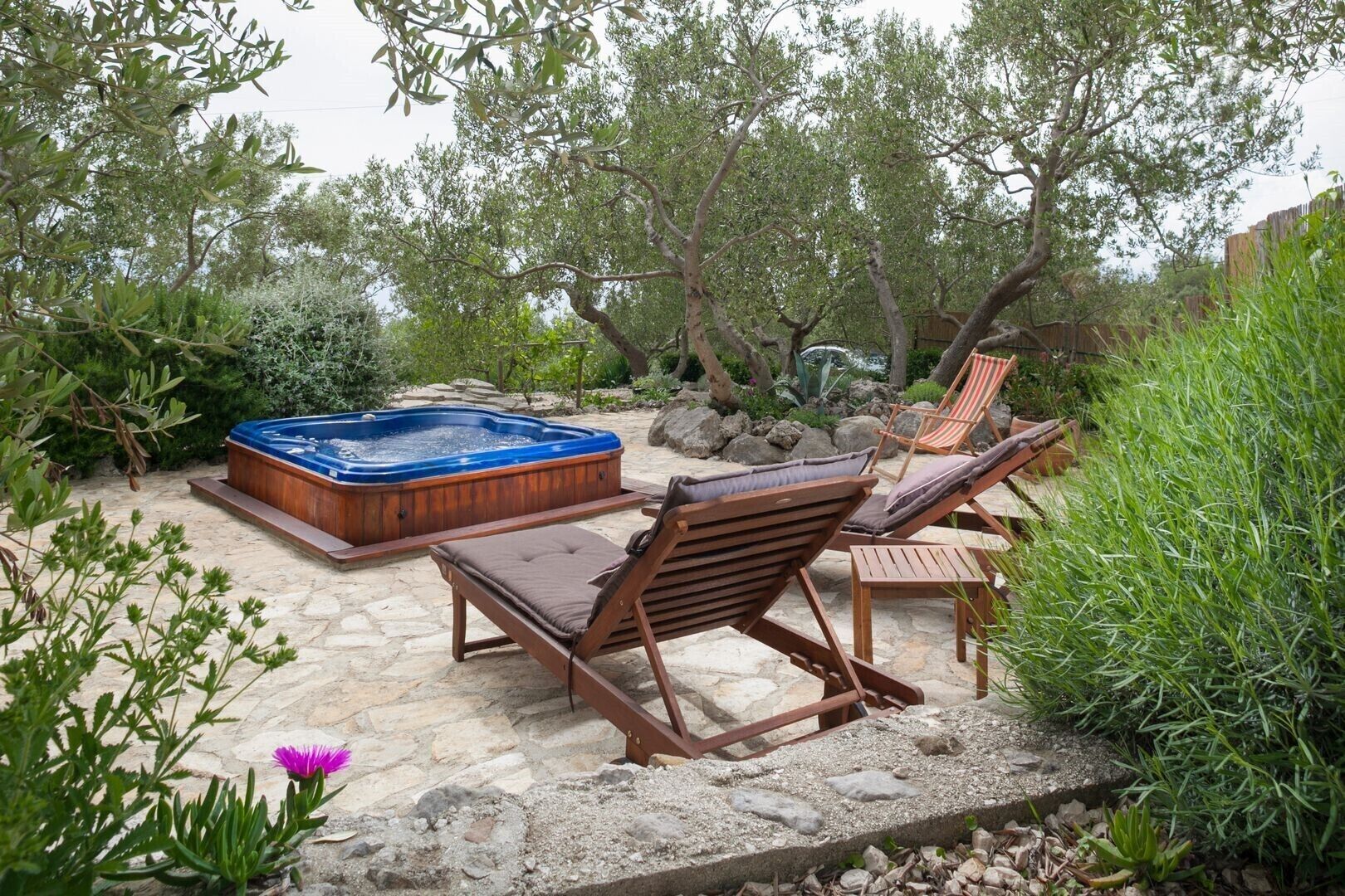Un bain à remous entouré de meubles de patio en pierre et d’une végétation luxuriante.
