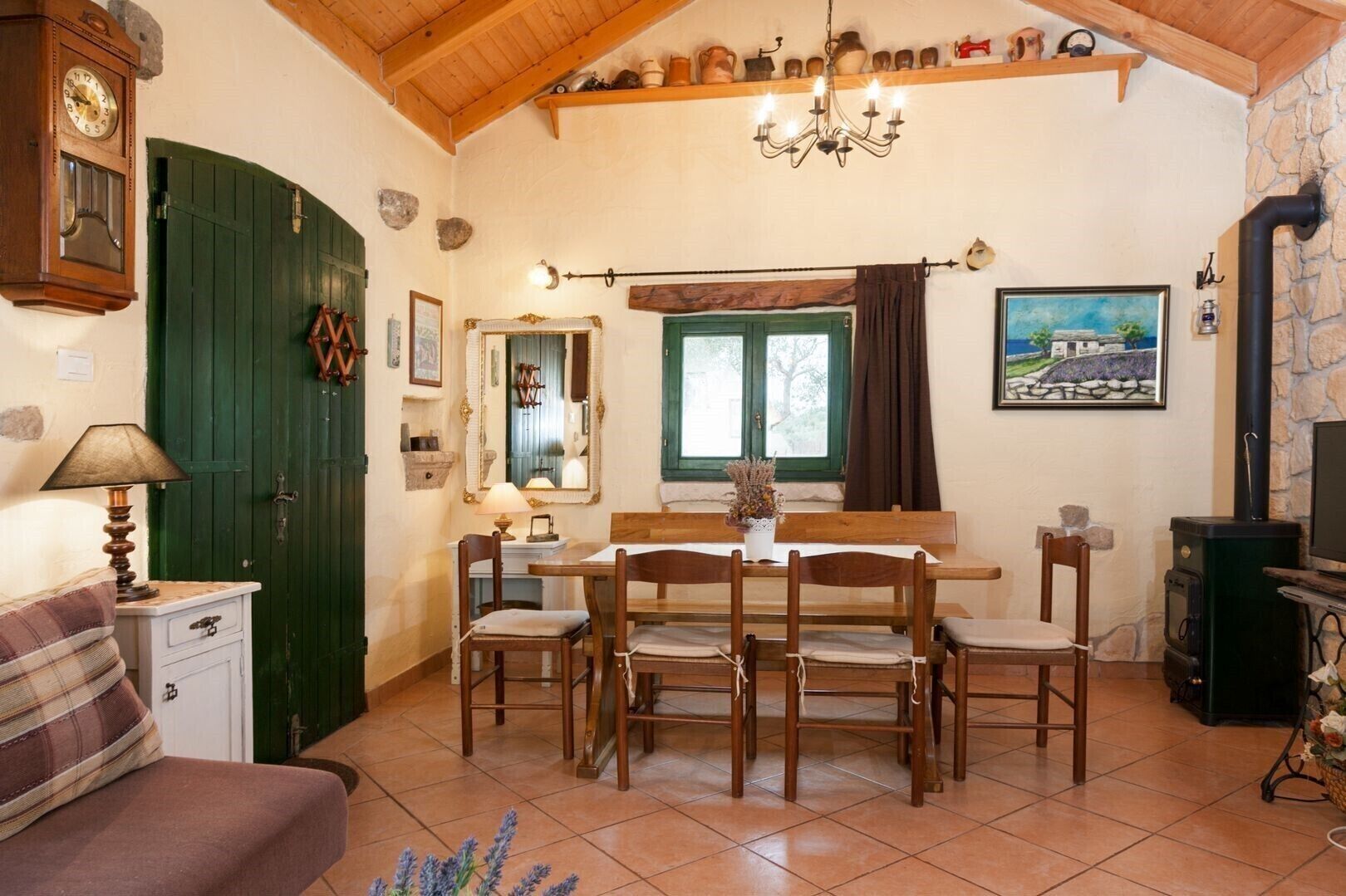 A cozy dining area with a wooden table and chairs, a green door, a wall clock, and a painting.