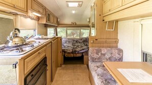 Una cocina compacta para autocaravana con armarios de madera, estufa y comedor con mesa y sofá.