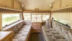Un interior de caravana acogedor, con dos zonas de asientos acolchados, una mesa central y armarios de madera.