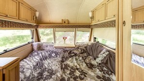 Interior acogedor de una casa rodante, con cama, una mesita y ventana que ofrece vistas a la vegetación.