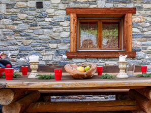 Een stenen muur met een houten raam en een picknicktafel met rode bekers en een schaal fruit.