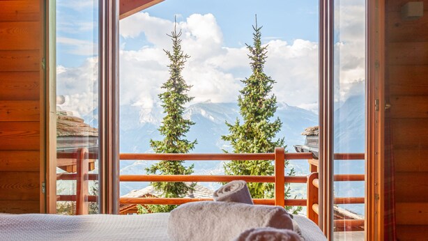 A wooden cabin room with a large window overlooking a mountain landscape.
