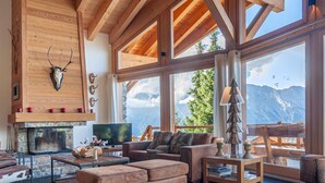 A spacious living room with a stone fireplace, leather furniture, and large windows offering mountain views.
