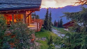 A wooden cabin with a stone roof, surrounded by trees and mountains.