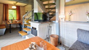 Een moderne woonkamer met een televisie, houten meubels, een trap en een raam met gordijnen.