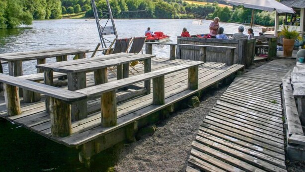 Een houten steiger met banken, een bootje en een gebouw met een parasol.