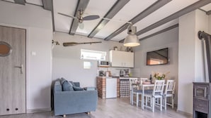 A modern living room with a grey sofa, a dining area with white chairs, a kitchen with white cabinets, and a fireplace.