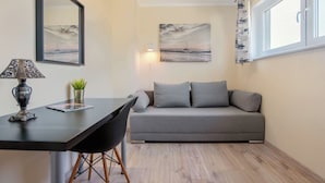 A modern living room with a grey sofa, a black dining chair, a table with a lamp, and two wall-mounted paintings.