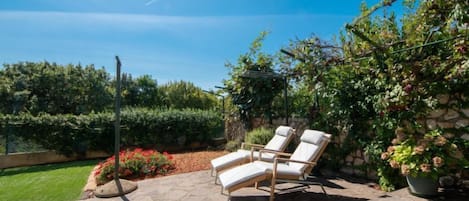 A patio with stone flooring, two lounge chairs, and a stone wall with climbing plants.