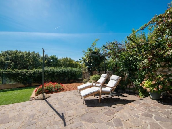 A patio with stone flooring, two lounge chairs, and a stone wall with climbing plants.