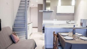 Eine moderne Küche mit Kochinsel, ein Essbereich mit Tisch für zwei Personen und eine Treppe, die zu einer anderen Ebene führt.