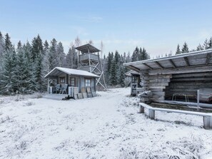 Een houten hutje met een sneeuwbedekte kap, een houten uitkijktoren en een blokhut met een metalen dak.
