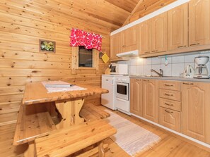 A wooden interior with a wooden table and bench, a kitchen with white appliances, and wooden cabinets.