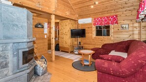 Et hyggeligt interiør i en træhytte med en stenspir, et fjernsyn og en rød sofa.
