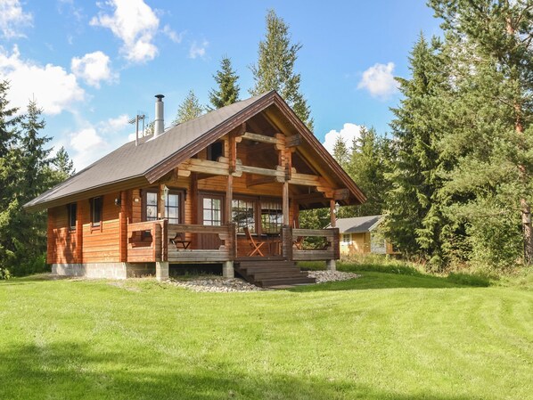 A wooden cabin with a porch, surrounded by a grassy area and trees.