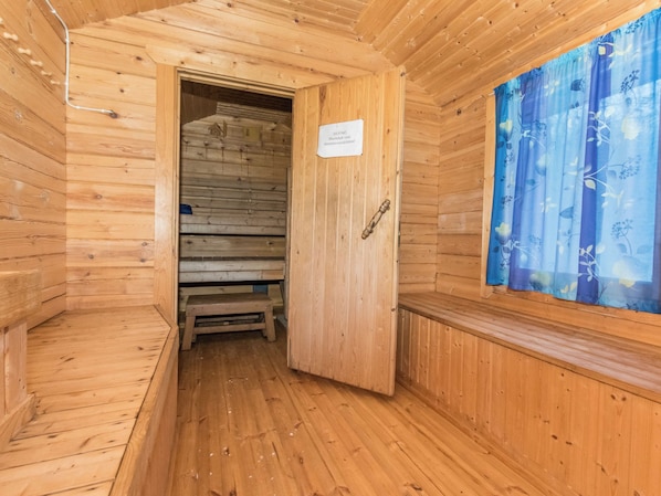 A wooden sauna room with a bench, a door with a sign, and a window with a curtain.