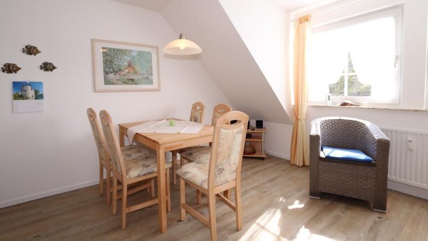 Un coin repas avec une table et des chaises en bois, un luminaire suspendu et une fenêtre avec des rideaux.