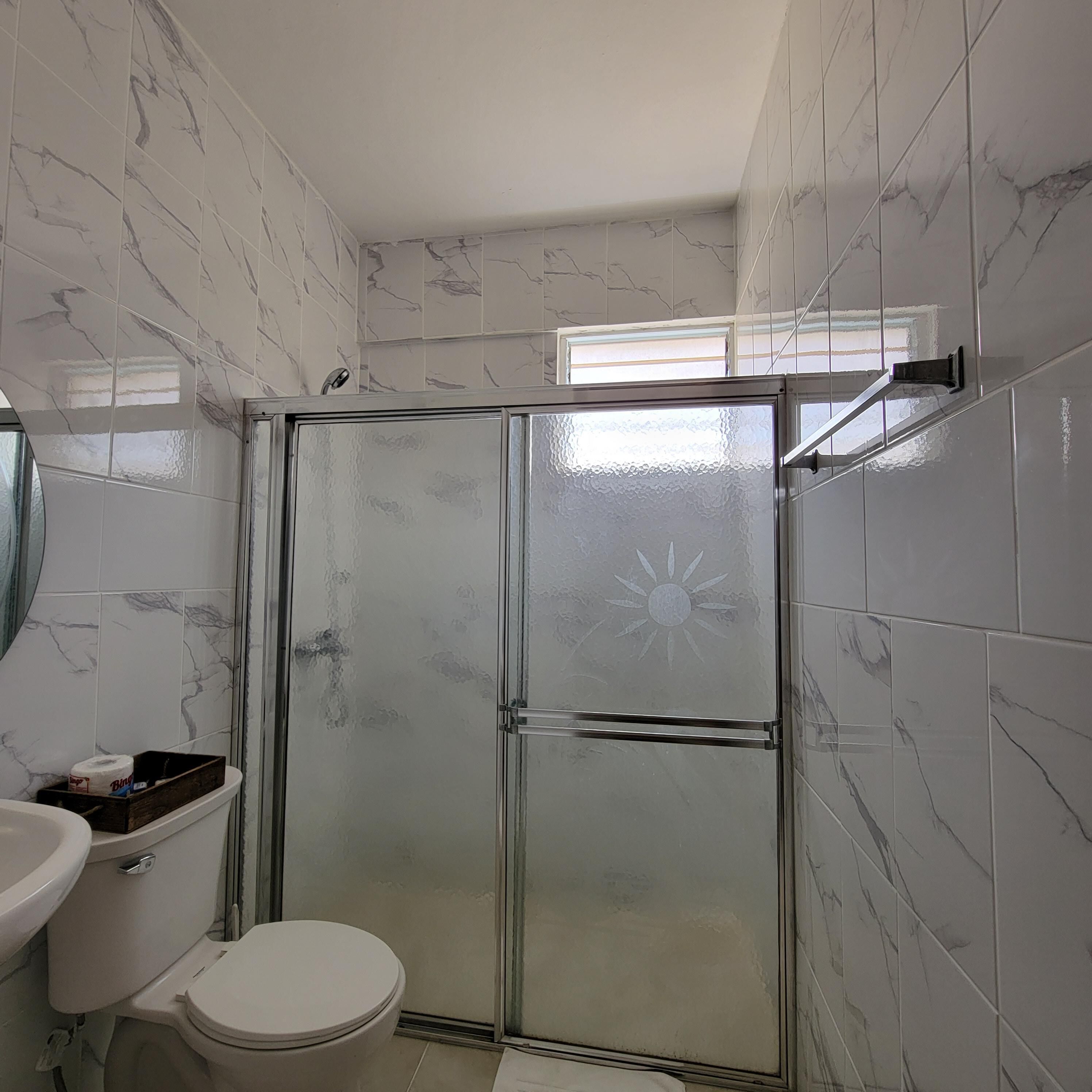 A bathroom with a glass shower enclosure, white toilet, and marble-patterned walls.