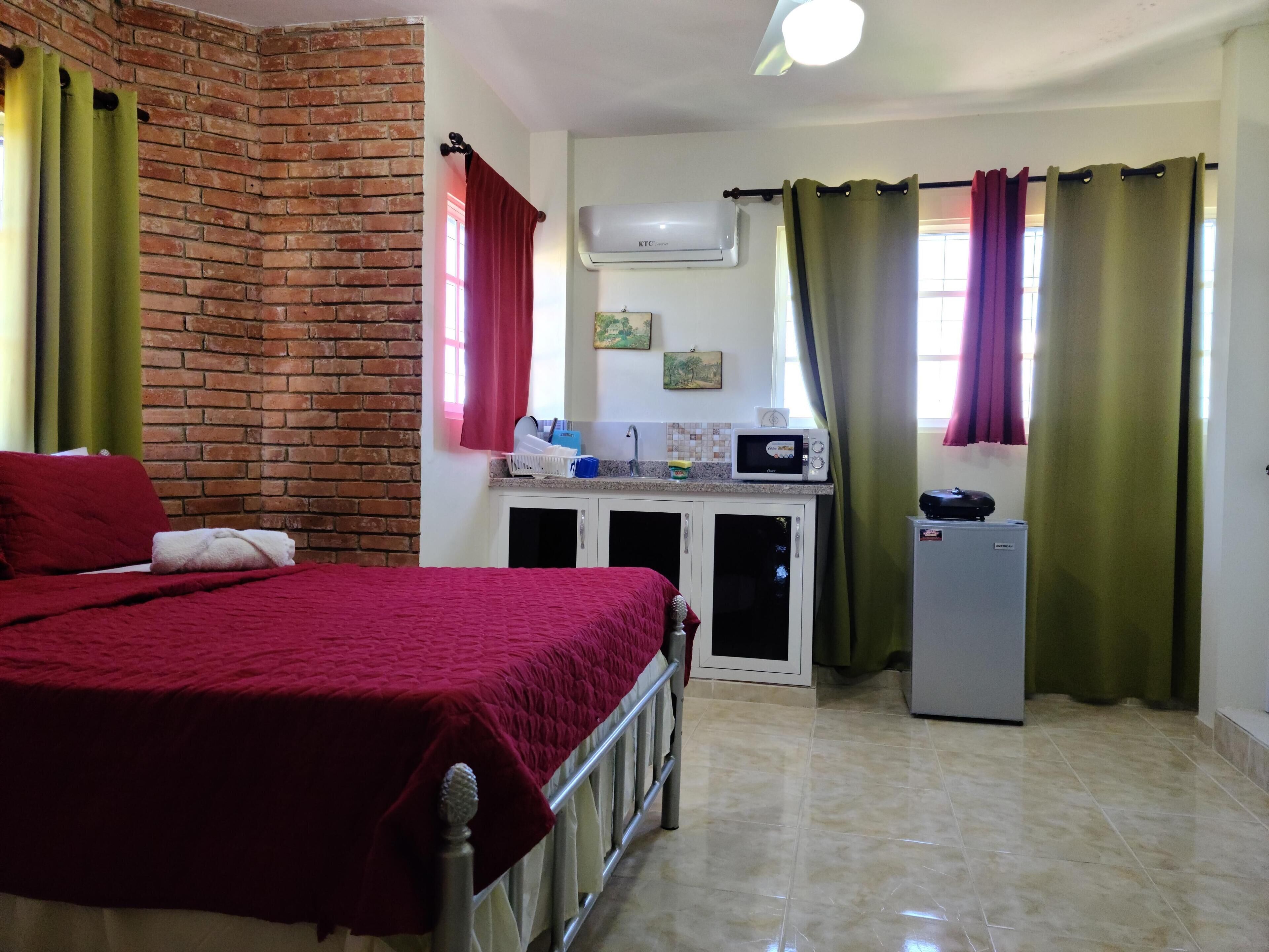 A bedroom with a bed, a small kitchenette with a microwave, and a refrigerator.