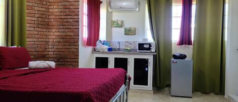 A bedroom with a bed, a small kitchenette with a microwave, and a refrigerator.