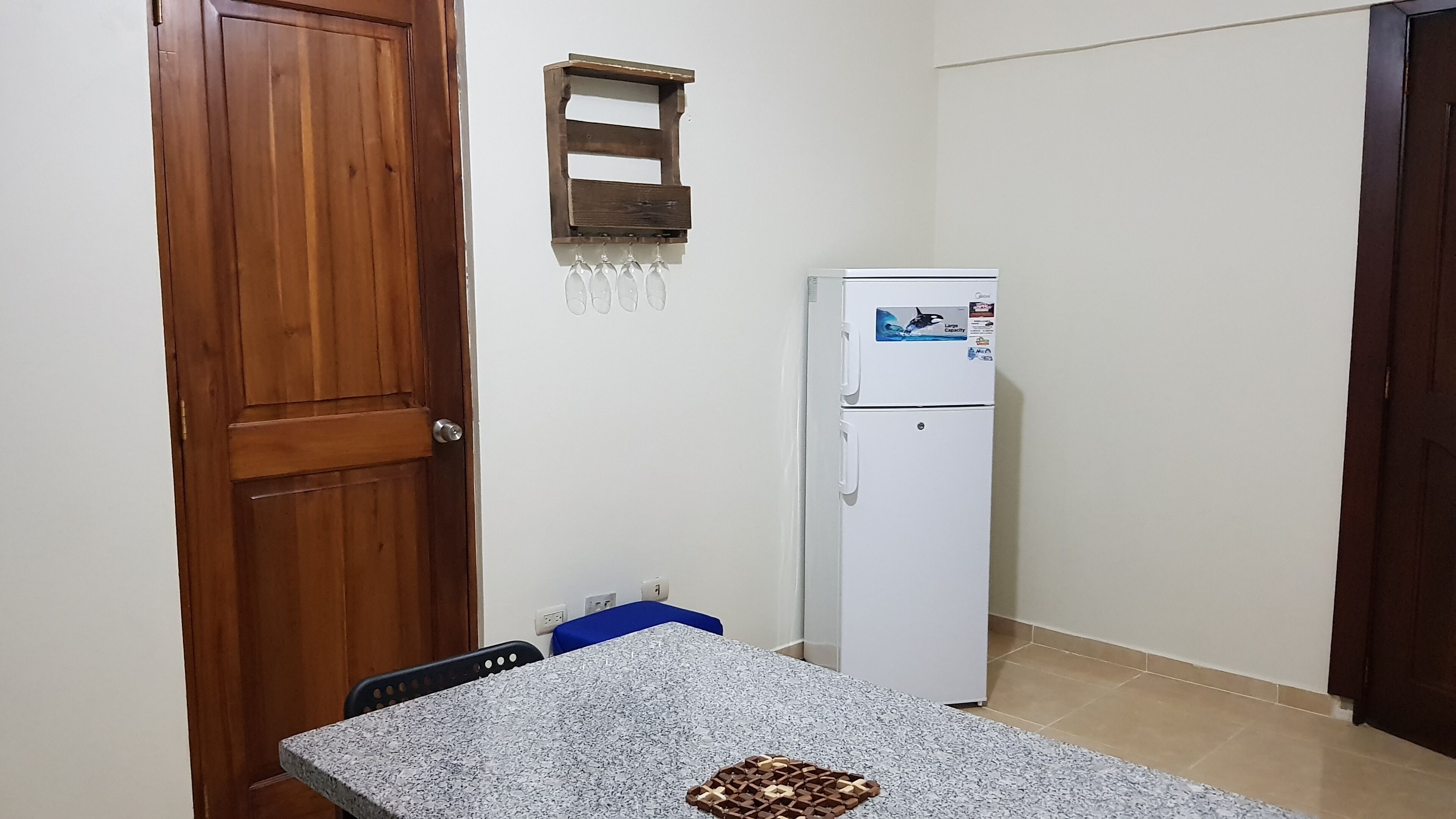 Una piccola cucina con una porta in legno, un frigorifero bianco, una sedia blu e un piano di lavoro in granito.