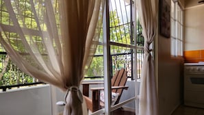 A balcony with a chair and table, a window with curtains, and a kitchen area with an oven. - Hotel Quinto Nivel RD (Salcedo)