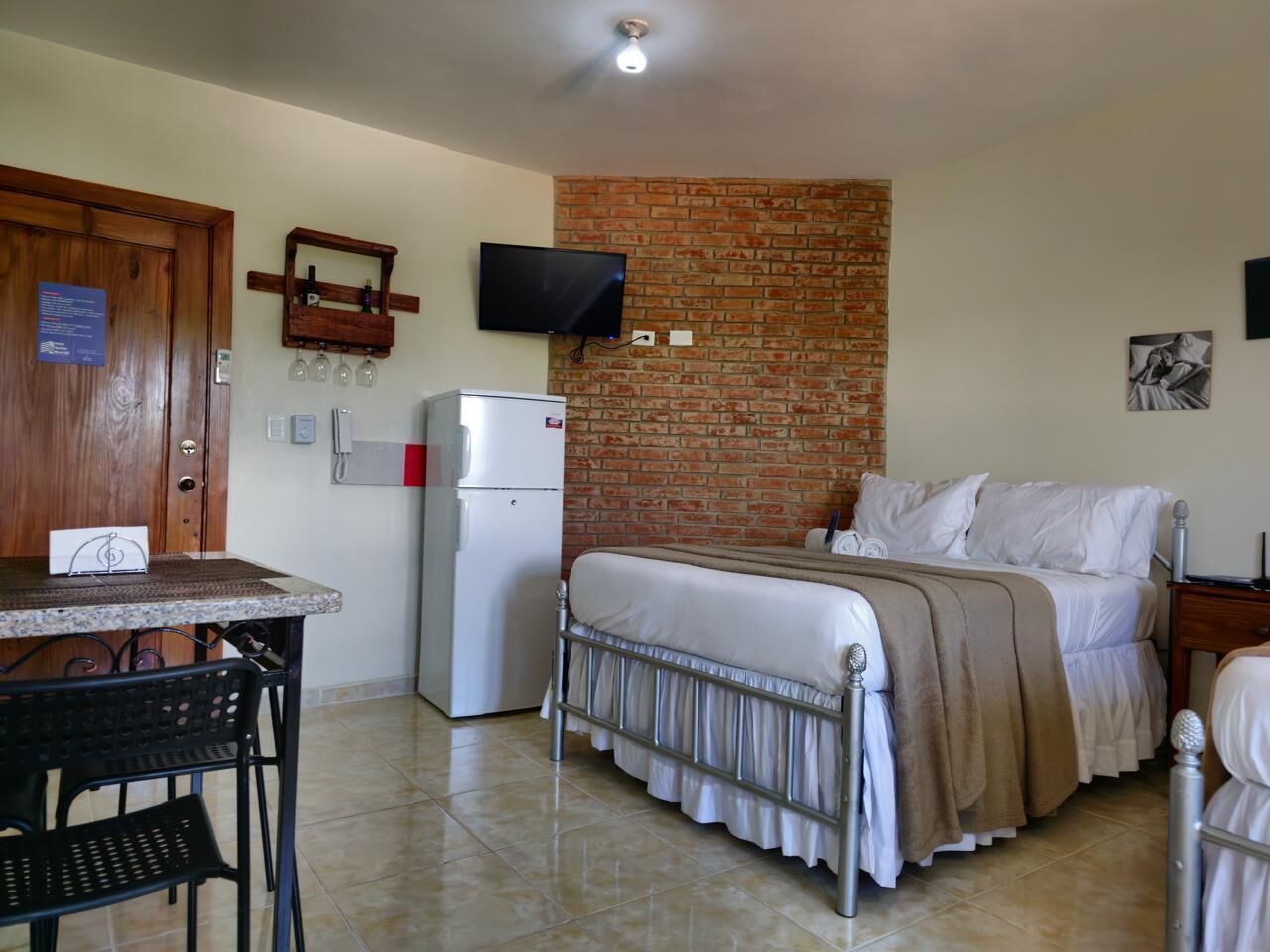 A bedroom with a brick wall, a bed, a TV, and a refrigerator.