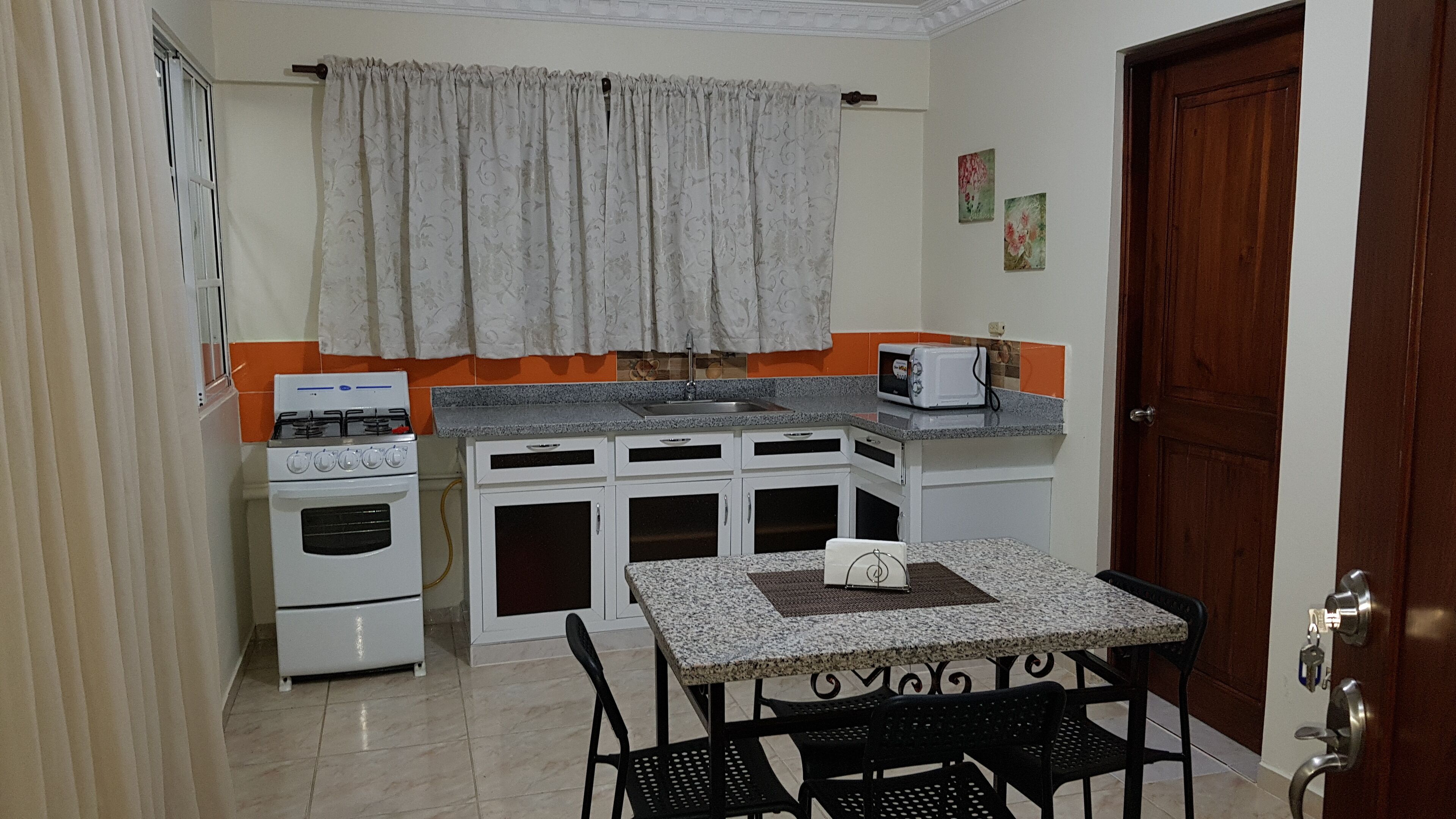 Una cocina compacta con estufa a gas, horno, microondas y una pequeña mesa con sillas.