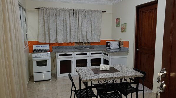 A compact kitchen with a gas stove, oven, microwave, and a small dining table with chairs. - Hotel Quinto Nivel RD (Salcedo)