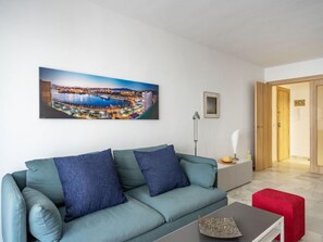A modern living room with a teal sofa, a red ottoman, and a cityscape painting on the wall.