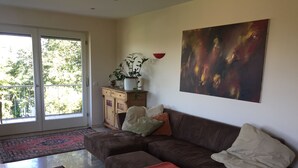 A living room with a brown leather sofa, a red throw blanket, and a large abstract painting on the wall.