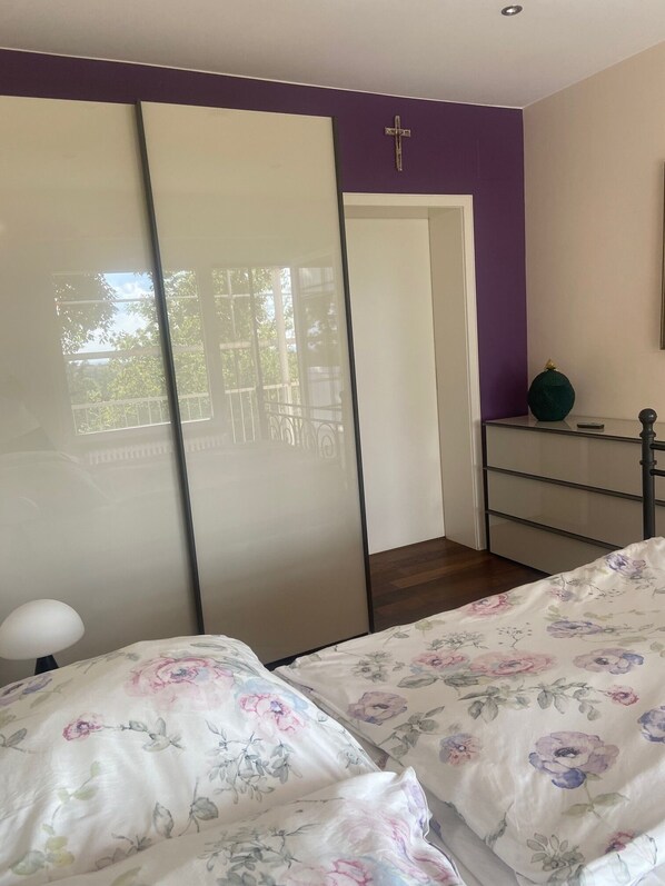 A bedroom with two beds, a wardrobe, a dresser, and a cross on the wall.