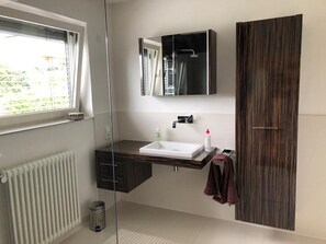 Ein modernes Badezimmer mit einer Duschkabine aus Glas, einem weißen Waschbecken und einem dunklen Holzschrank.