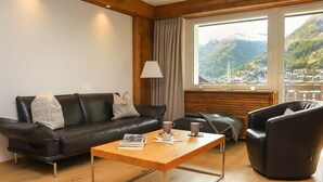A modern living room with a leather sofa, a wooden coffee table, and a leather armchair. A large window offers a view of a mountainous landscape. - Dianthus by Interhome (Zermatt)