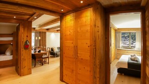 A spacious room with wooden floors and walls, a dining area with a table and chairs, and a bed with towels. - Dianthus by Interhome (Zermatt)