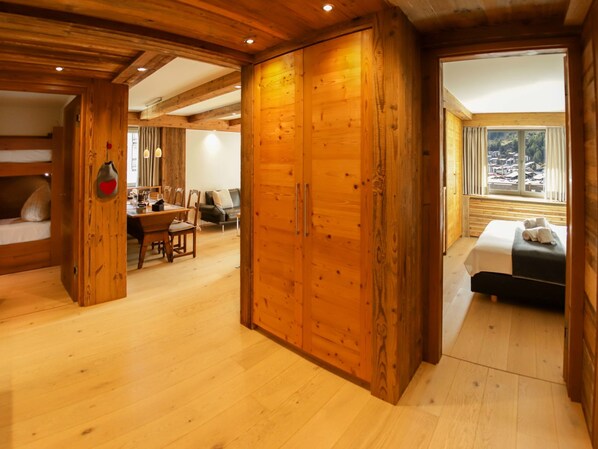 A spacious room with wooden floors and walls, a dining area with a table and chairs, and a bed with towels.