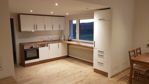 A modern kitchen with white cabinets, a built-in oven, a sink, and a window overlooking a forested area.