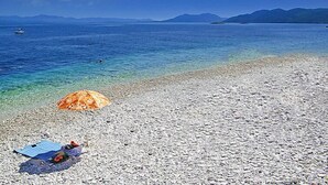 A pebble beach with a clear blue sea, a boat in the distance, and a beach umbrella.