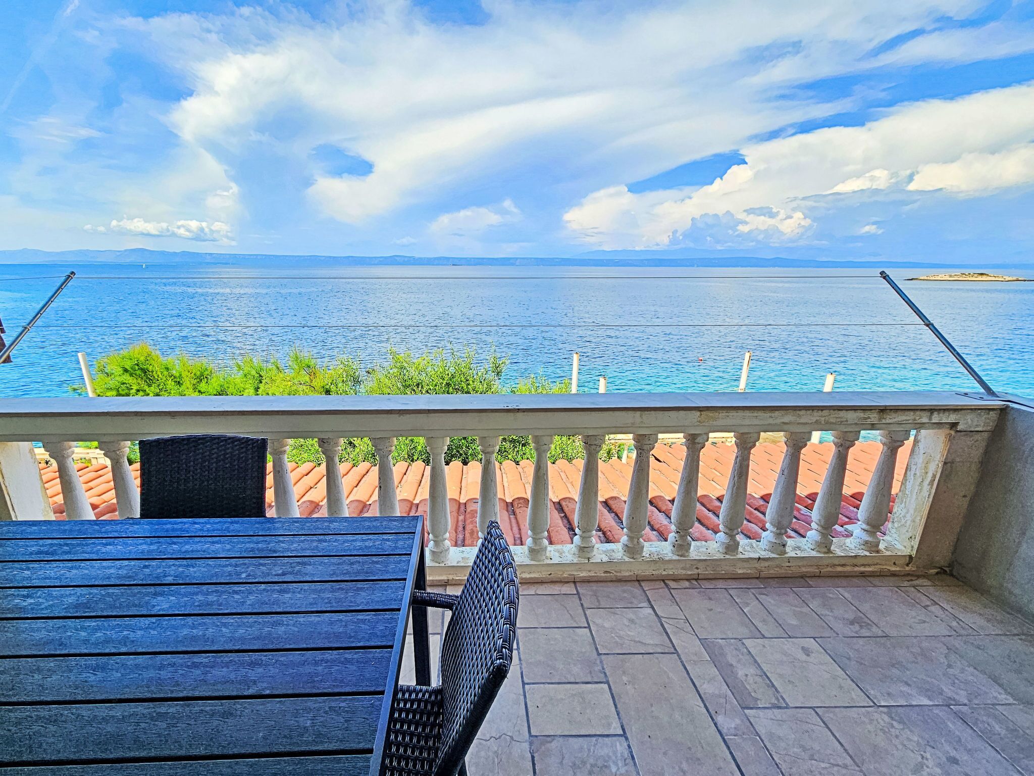 A balcony with a view of the sea, a table, and a chair.