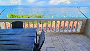 A balcony with a view of the sea, a table, and chairs.