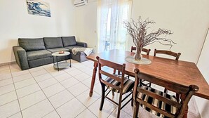 A living room with a sofa, a coffee table, a dining table with chairs, and a vase with branches.