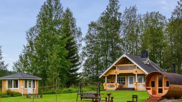 En hytte med veranda og gyngestativ, omgivet af en sø og træer.