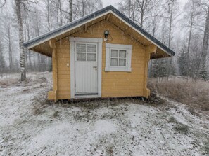 A small wooden cabin with a white door and window, surrounded by snow-covered ground and trees. - Kissaniemi by Interhome (Iisalmi)