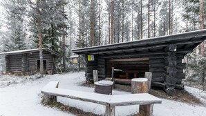 En rustik hytte med en træbænk og et bålsted i sneen.